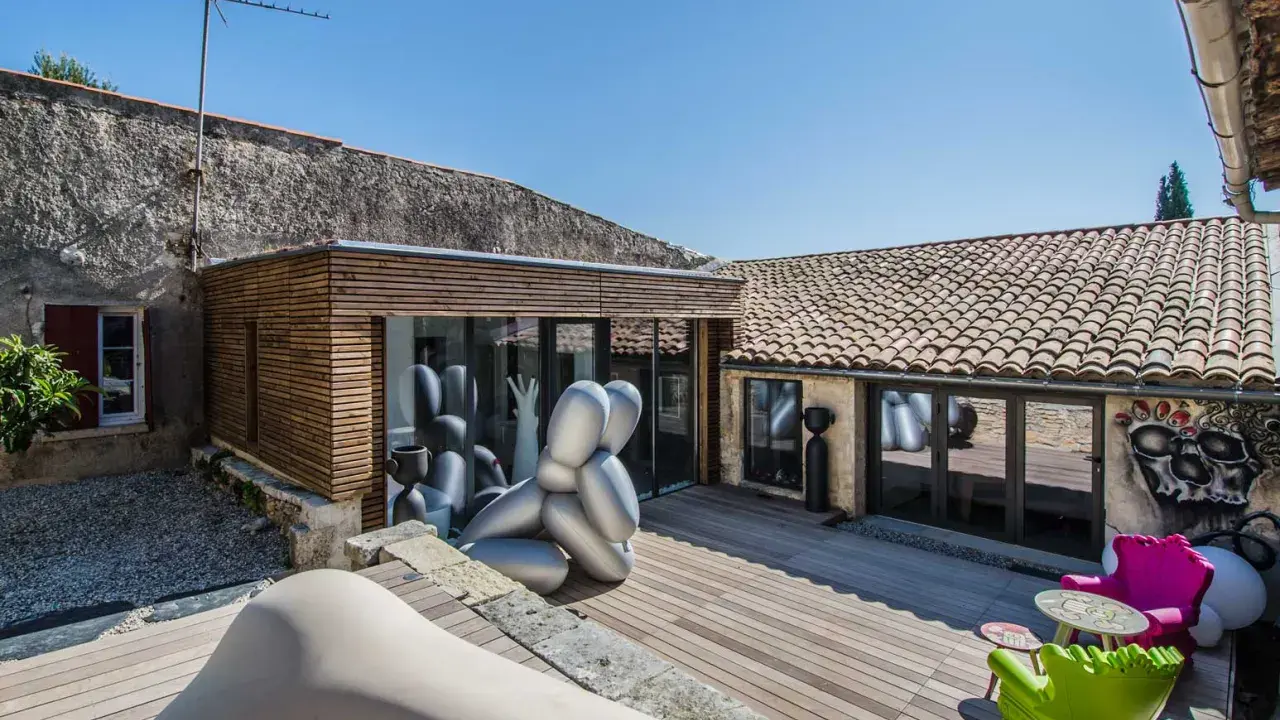 Extension maison ancienne architecte : une cour avec sculptures modernes, mobilier coloré et une extension en bois et verre.