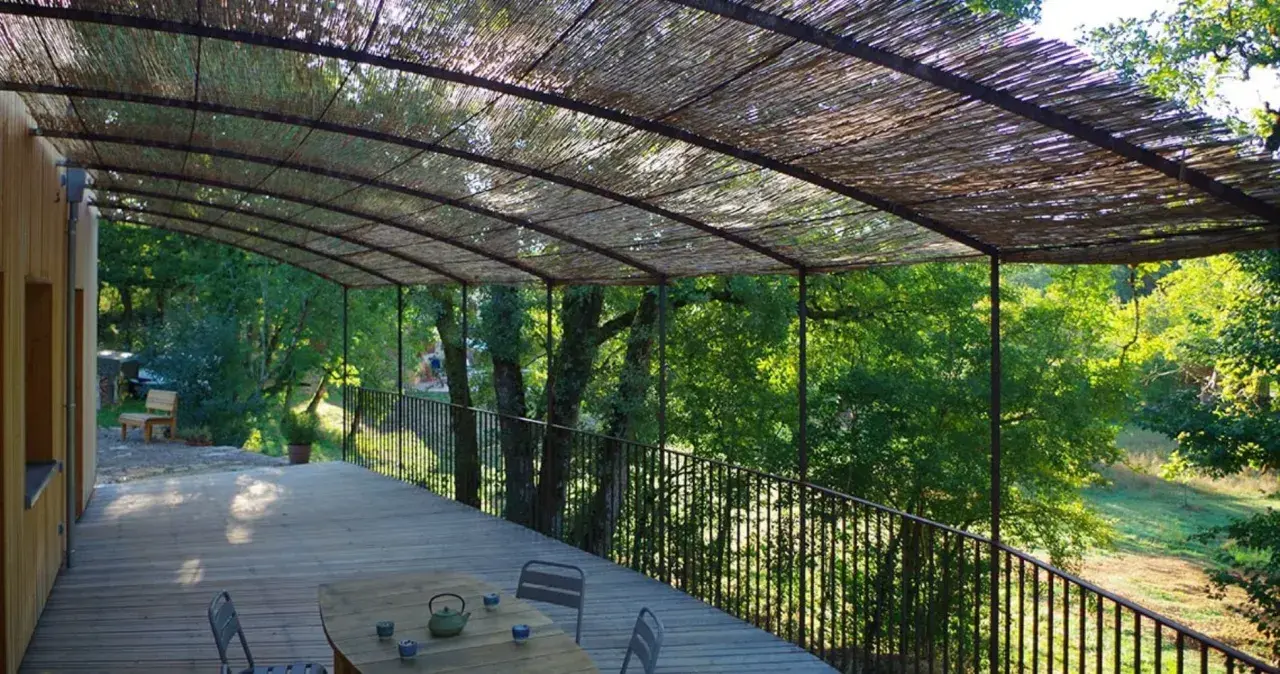 Vue d'une terrasse en bois sous une pergola recouverte de canisse. Le sens de pose de canisse sur pergola offre une ombre naturelle et agréable.