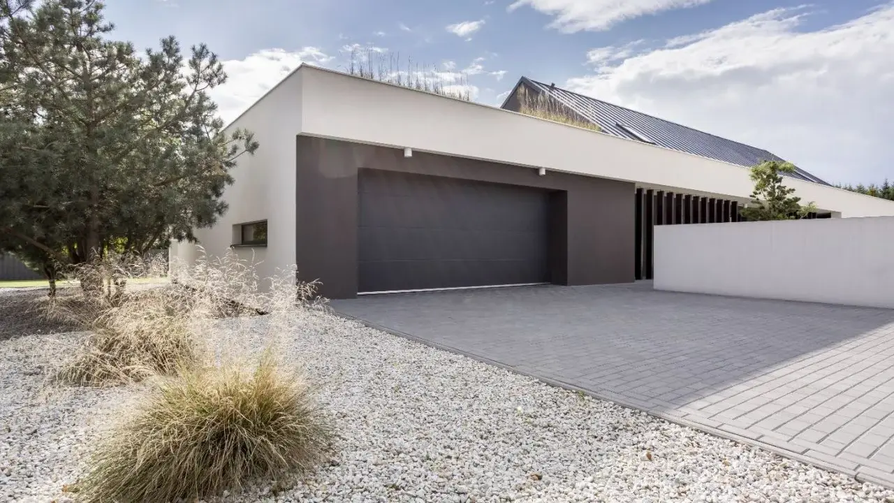 Moderne maison avec agrandissement garage, allée pavée, gravier blanc et végétation.