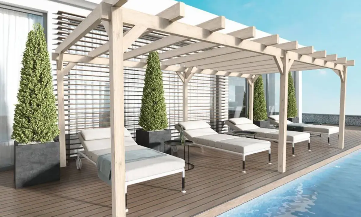 Une **pergola bois** avec des canisses protège des chaises longues au bord d'une piscine.