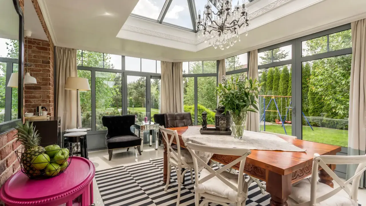 Une élégante veranda couloir avec un lustre, une table en bois et des fauteuils, donnant sur un jardin verdoyant.