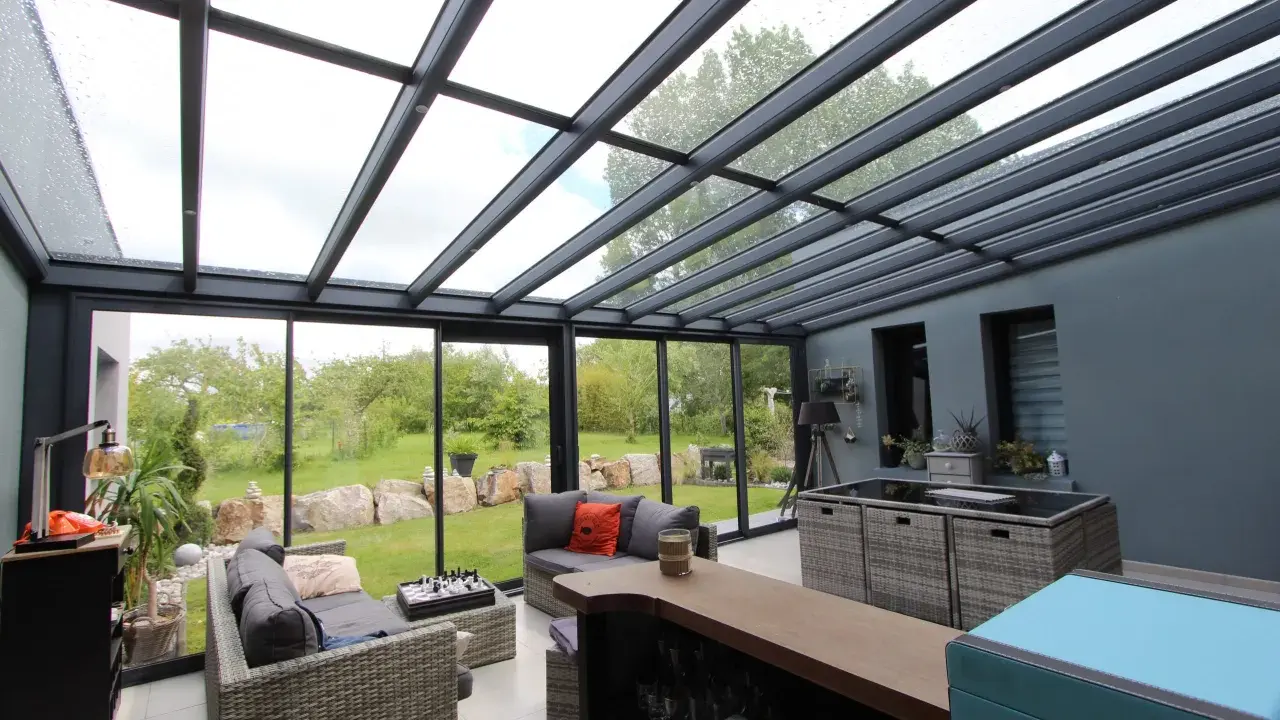 Salon moderne avec un toit en verre laissant entrer la lumière. Des canapés confortables invitent à la détente, tandis que le jardin verdoyant offre une vue paisible.