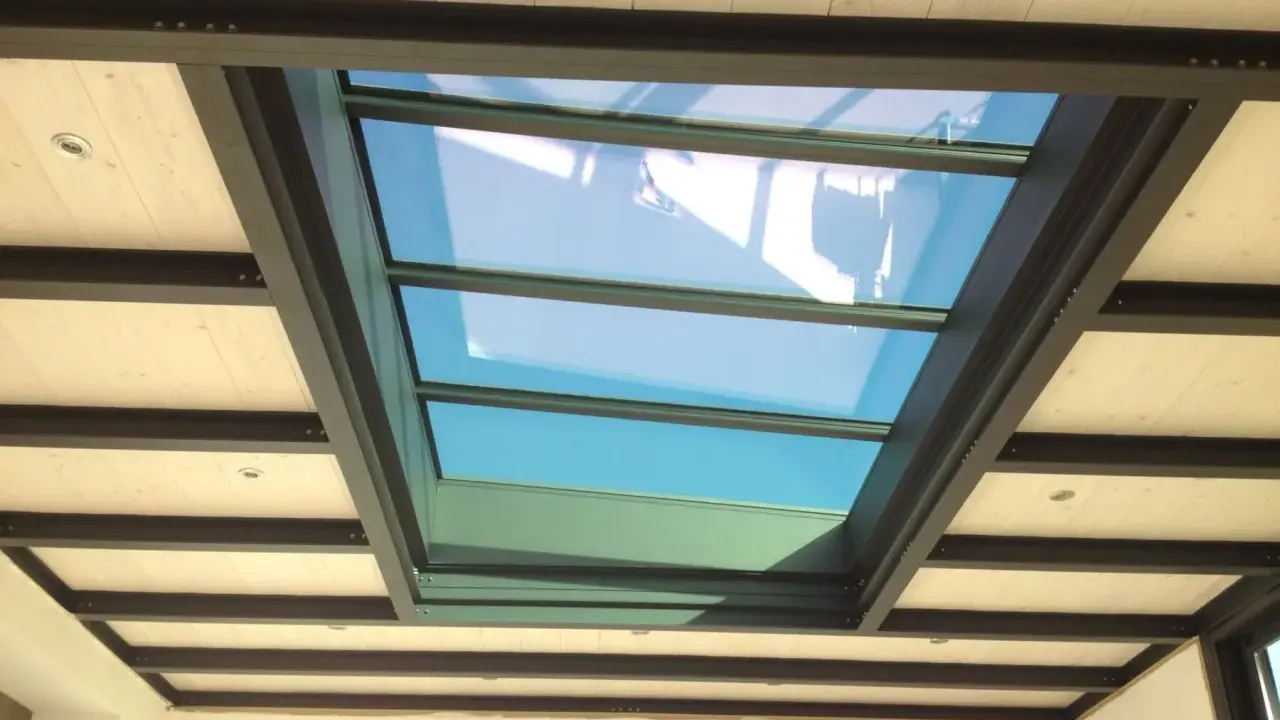Veranda avec un grand puit de lumière vitré, illuminant un plafond en bois et poutres métalliques.