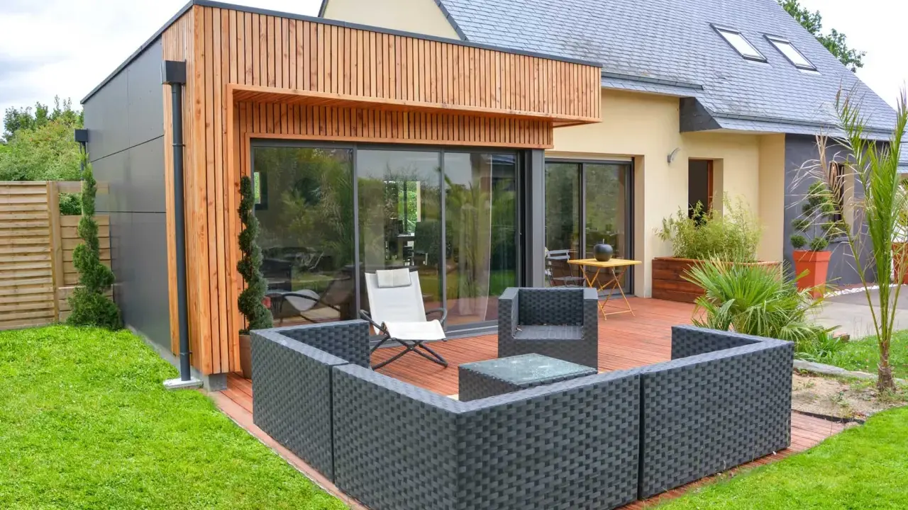 Une extension bois 30m2 moderne avec terrasse en bois, mobilier de jardin et grandes baies vitrées.