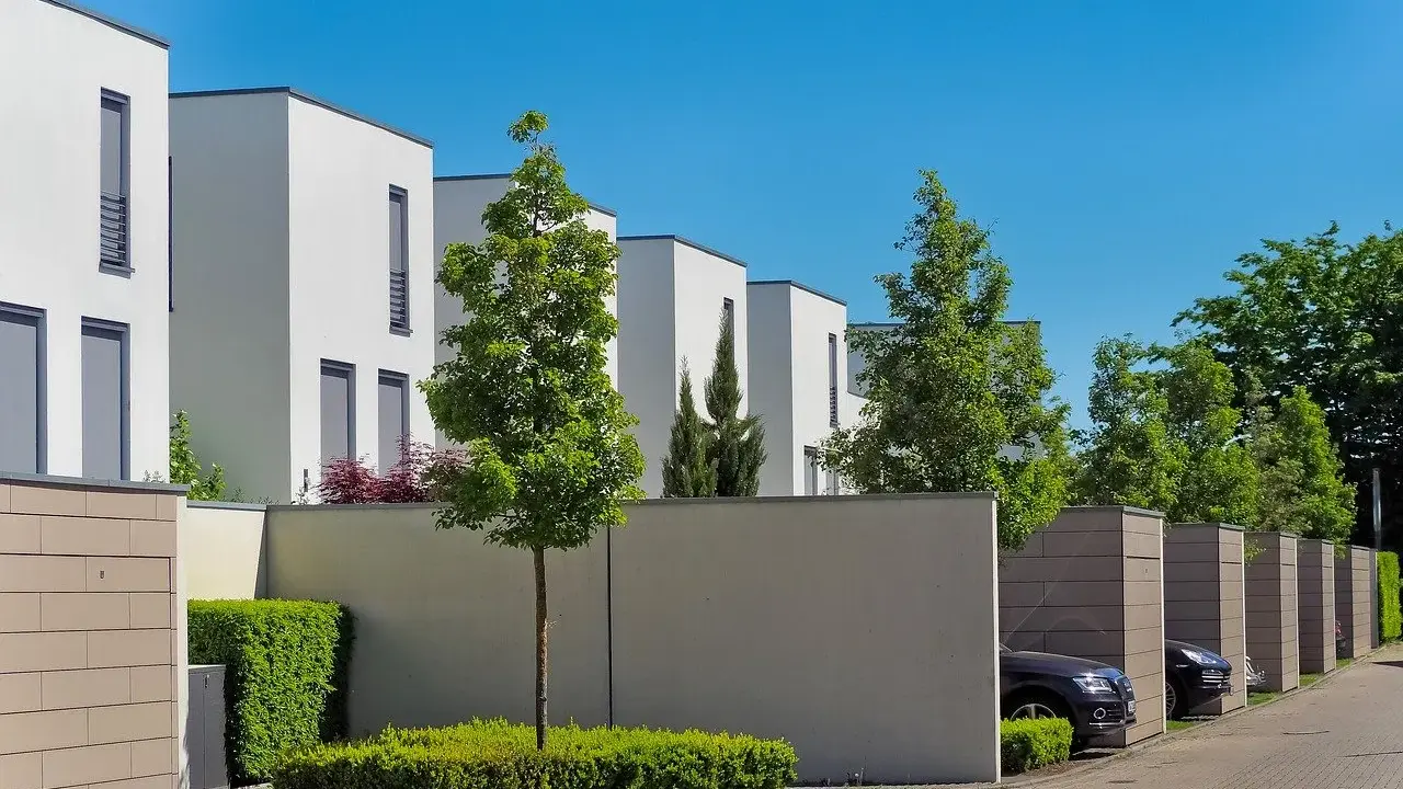 Lignes architecturales modernes, une extension accolée sur mur non mitoyen, des arbres et des voitures garées dans des box.
