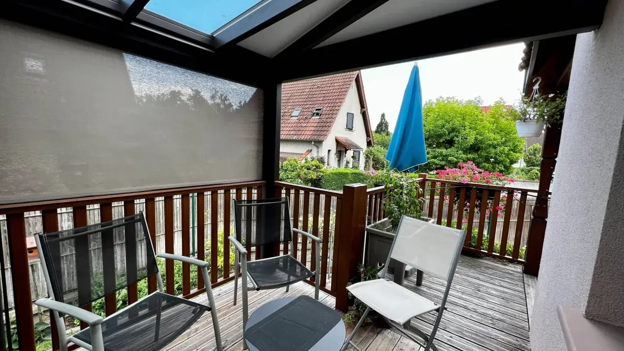 Un petit veranda balcon avec des chaises et une table, offrant une vue sur un jardin verdoyant et une maison.