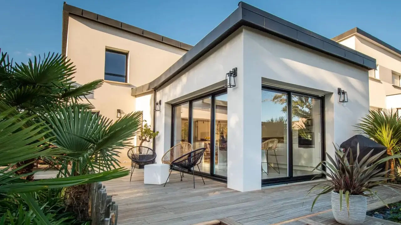Une extension verrière moderne illumine cette maison ancienne, offrant une vue imprenable sur la terrasse en bois et le jardin luxuriant.