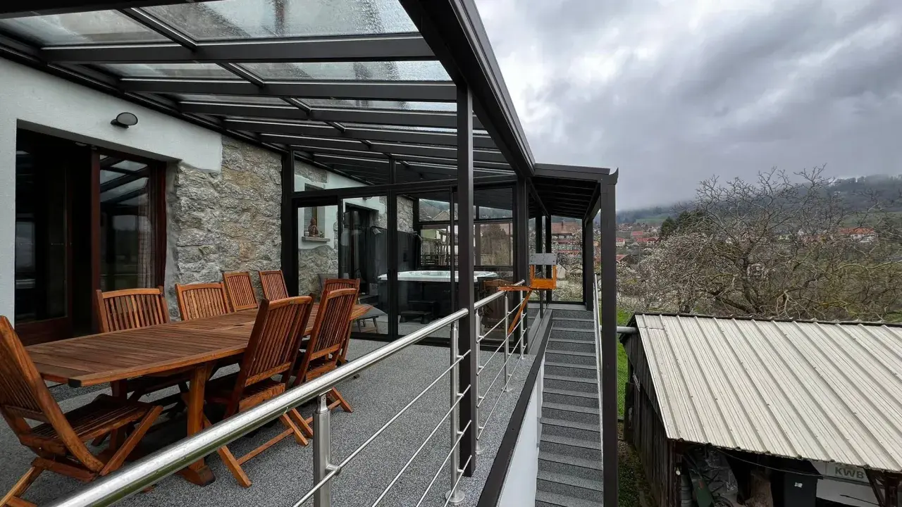 Veranda sur terrasse surélevée avec jacuzzi et table en bois. Vue sur un village et des collines brumeuses.