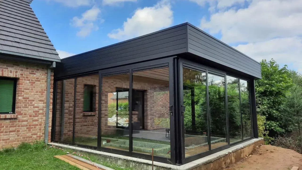 Moderne véranda toit plat avec puits de lumière, offrant une vue panoramique sur le jardin. L'extension en verre et métal s'intègre parfaitement à la maison en briques.