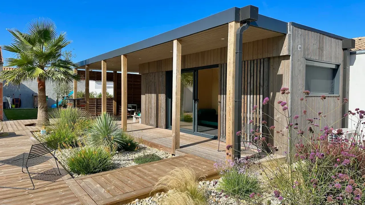 Maison moderne avec une extension toiture terrasse en bois, entourée d'un jardin paysager et d'une terrasse en bois.