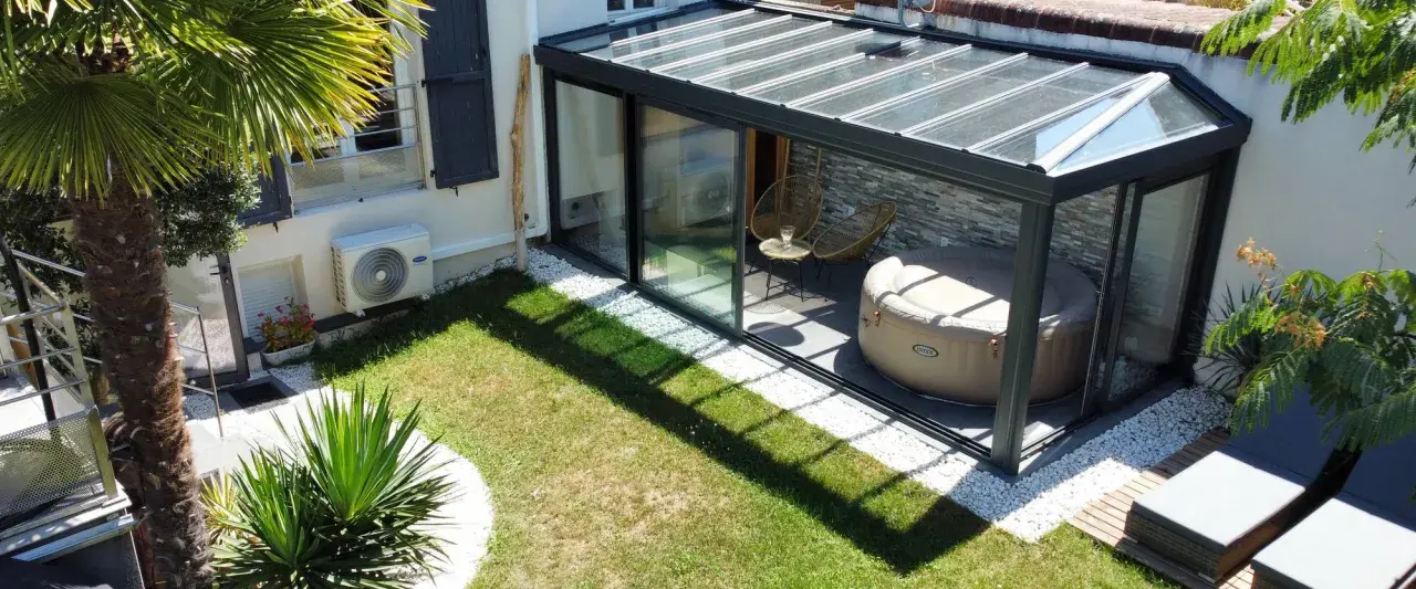 Une **veranda tuile** moderne avec jacuzzi et fauteuils, entourée d'un jardin verdoyant et d'une palme luxuriante.