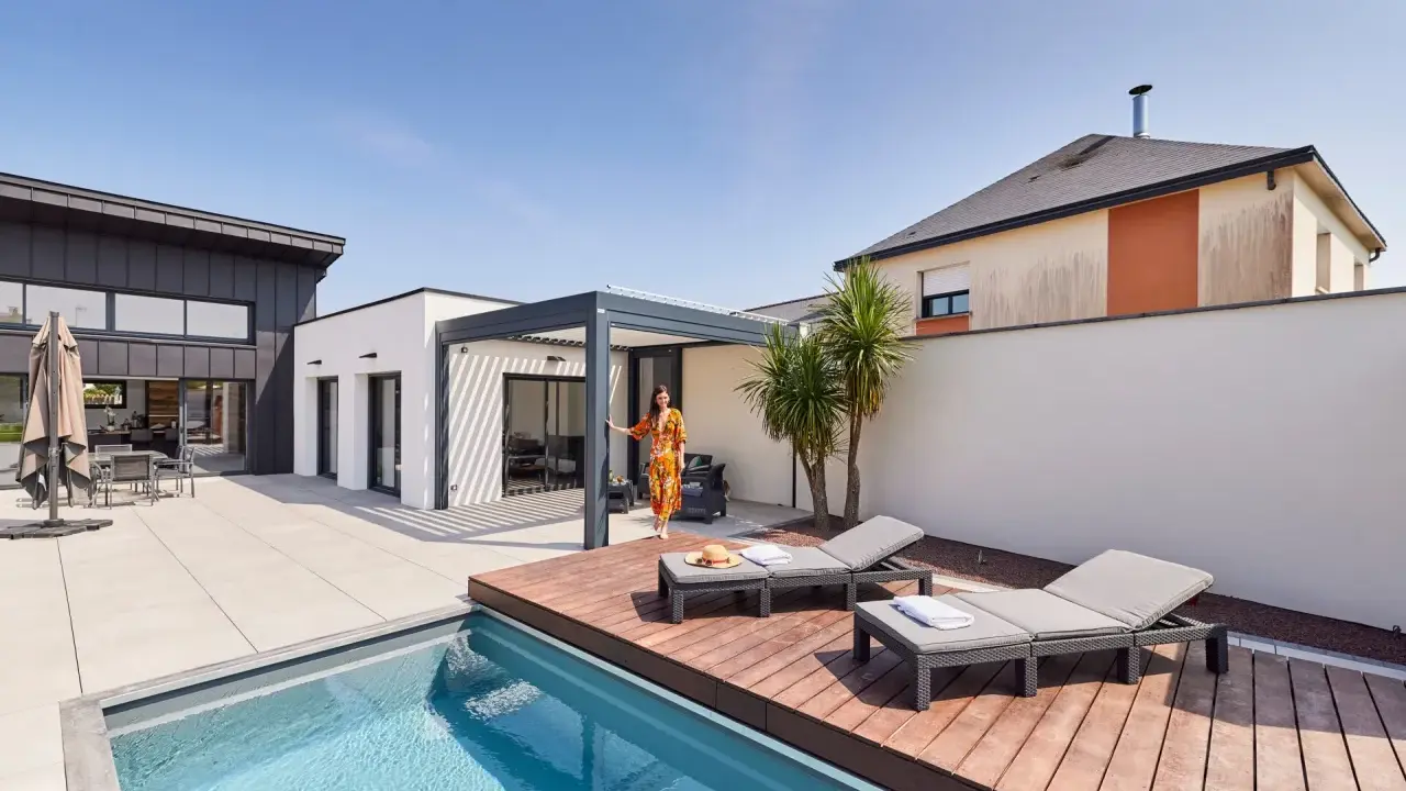 Une femme en robe colorée se tient près d'une pergola moderne, profitant de l'étanchéité pergola mur. Piscine et chaises longues complètent ce paysage de détente.