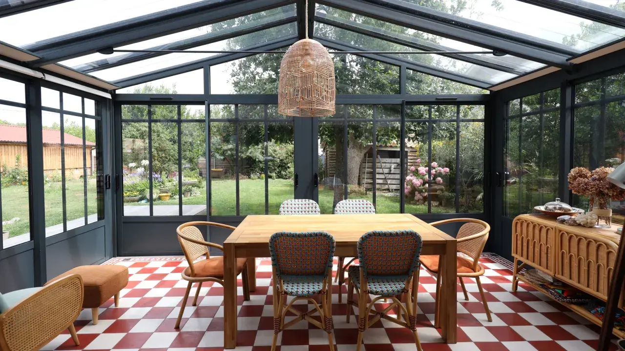 Salle à manger lumineuse dans une véranda extension, avec table en bois, chaises colorées et vue sur le jardin.
