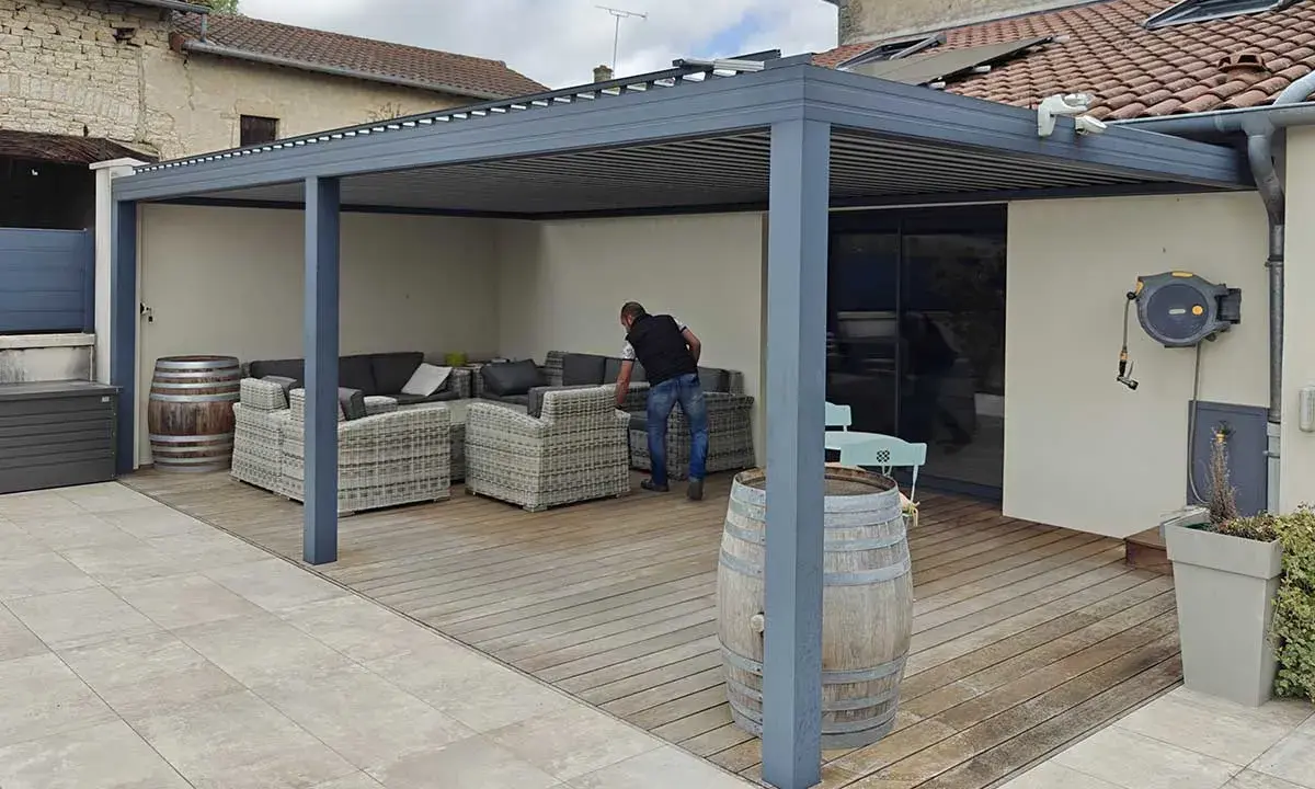 Installation d'un auvent sans permis de construire. Un homme arrange des coussins sur un canapé extérieur sous la structure moderne.