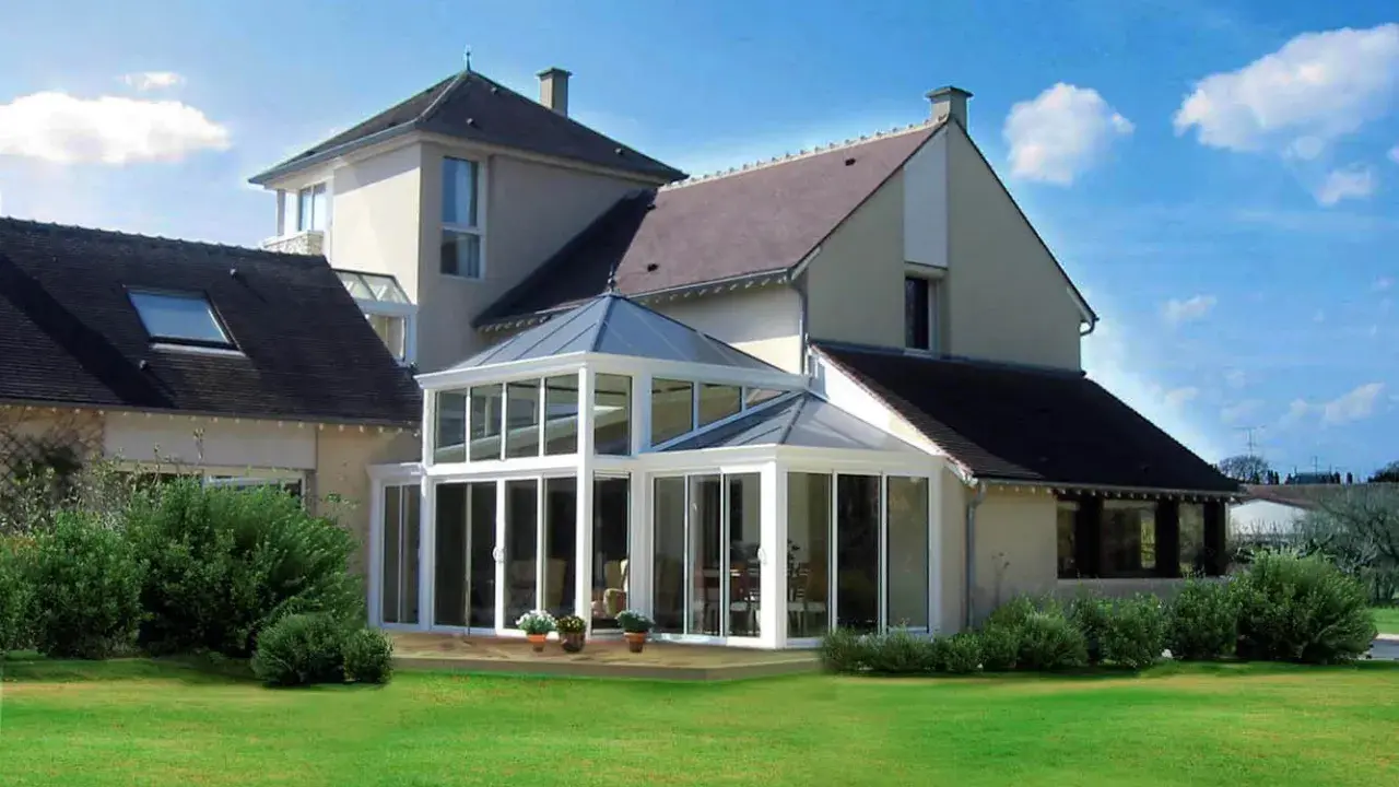 Une **veranda angle maison** moderne, avec une structure vitrée lumineuse, s'intègre parfaitement à l'architecture de la demeure.