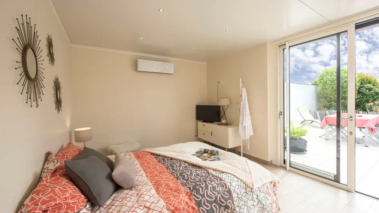 Chambre lumineuse d'une extension de maison, avec un lit confortable, une télévision et un accès direct à une terrasse extérieure.