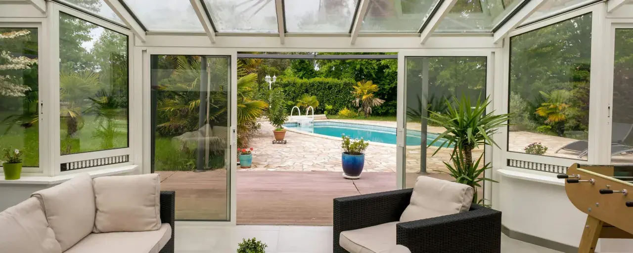 Une extension vitrée moderne s'ouvre sur une piscine et un jardin luxuriant, invitant à la détente.