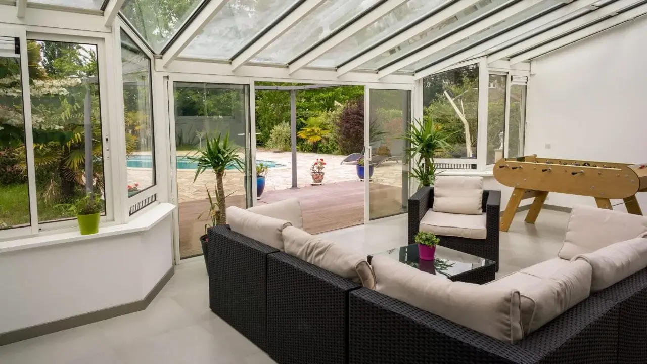 Vaste veranda 50m2 avec salon, baby-foot et vue sur piscine. Idéal pour se détendre et s'amuser en famille.