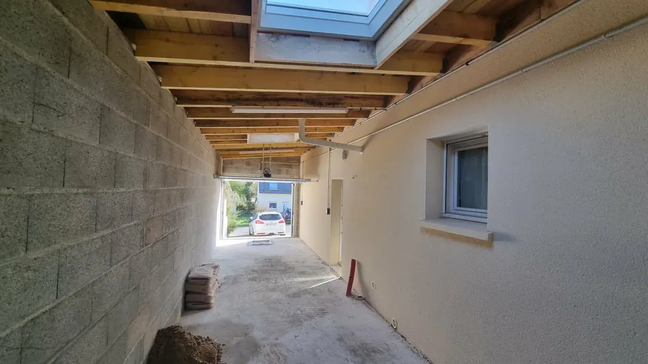 Couloir en construction, partie d'une extension maison, avec murs en parpaings, plafond en bois, fenêtre de toit et matériaux de chantier.