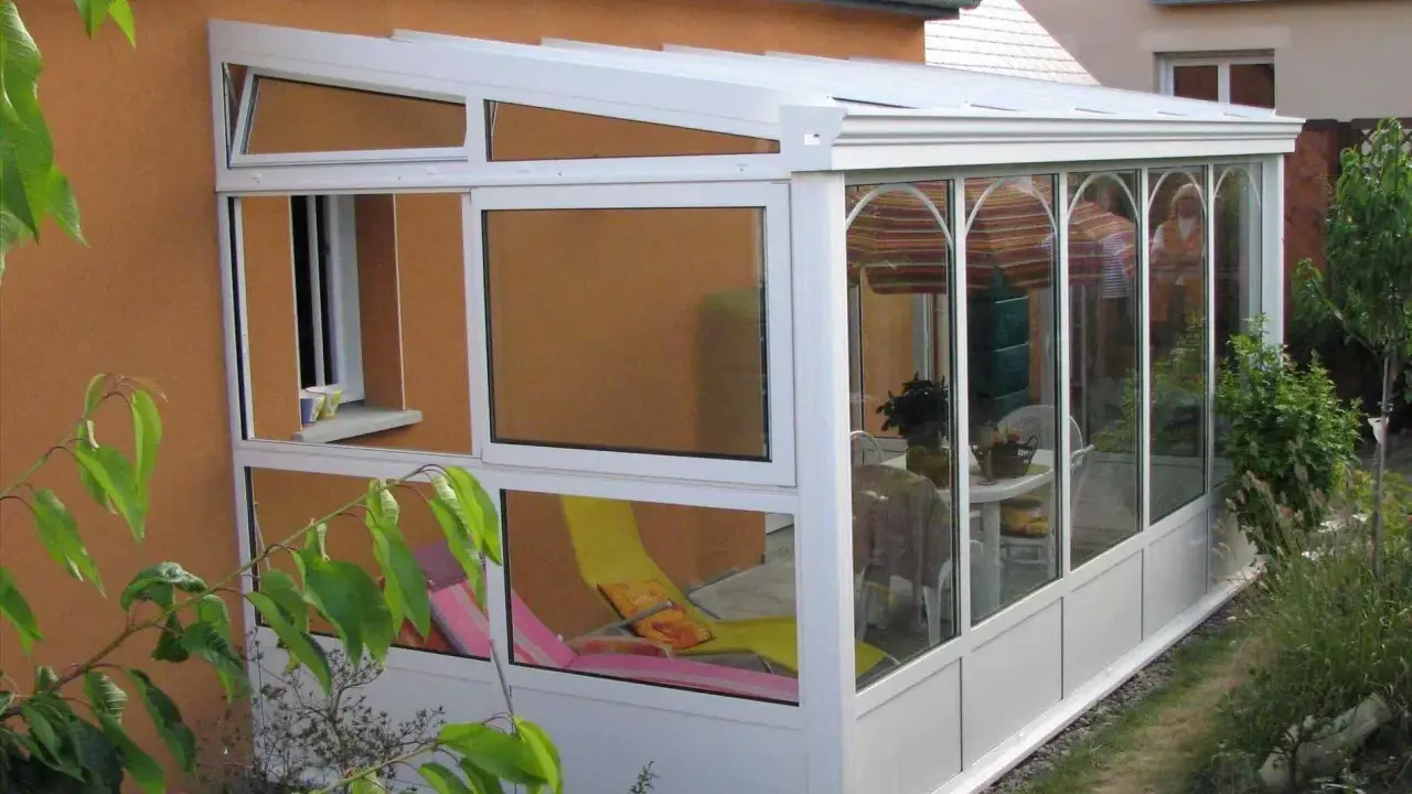 Une véranda démontable sans permis de construire, avec chaises longues et table à manger, prolonge la maison pour profiter du jardin.