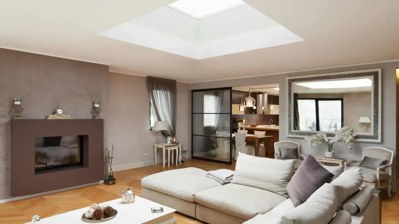 Un salon moderne avec un grand puit de lumière au plafond, un canapé confortable, une cheminée et une cuisine ouverte.