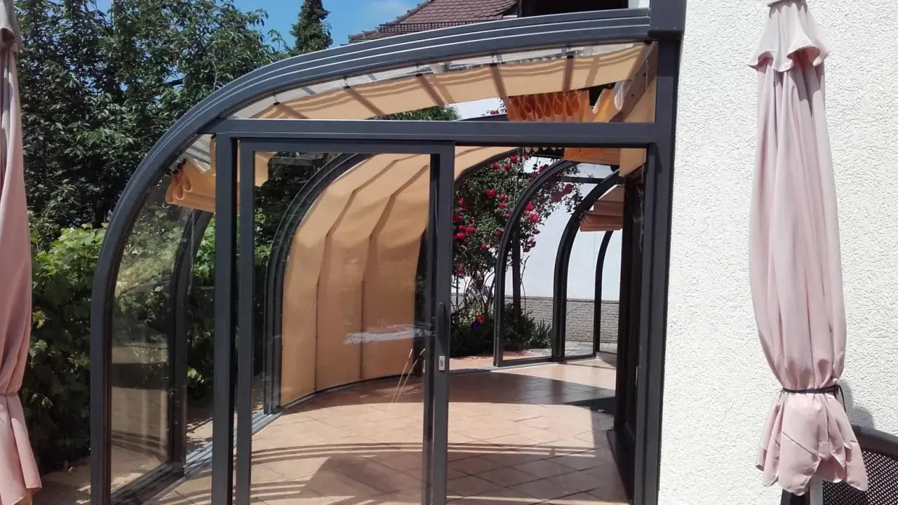 Une élégante veranda demi ronde en verre et métal, avec des stores rétractables, s'ouvre sur un jardin fleuri.
