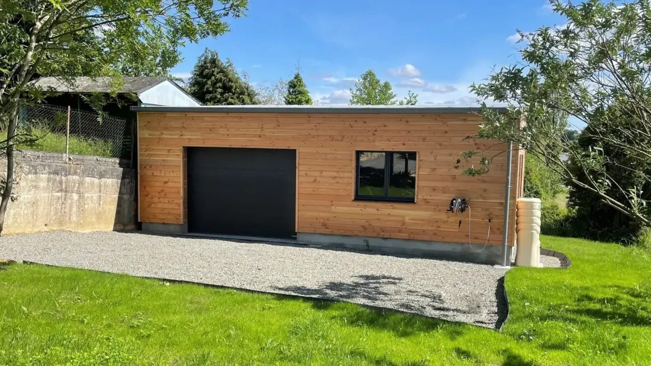 Extension garage bois accolé maison, avec porte noire, fenêtre et jardin verdoyant.