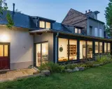Extension maison en L avec grandes baies vitrées illuminant un salon et une cuisine. Une porte rouge s'ouvre sur une terrasse pavée.