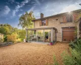 Maison en pierre avec une veranda lumineuse, un jardin de gravier et un paysage vallonné en automne.