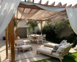 Une belle idée pergola jardin avec salon de jardin, chaises et table à manger, le tout sous des voilages légers.
