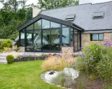 Maison avec extension toit vitrée, terrasse en bois et jardin fleuri.