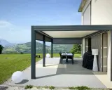 Pergola bioclimatique moderne face à un paysage vallonné. Le vent fort fait onduler les lames du toit, créant des jeux d'ombre et de lumière.