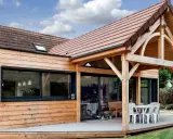 Extension de maison en bois avec terrasse sur dalle béton. Une table et des chaises sont installées sous un auvent.