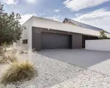 Moderne maison avec agrandissement garage, allée pavée, gravier blanc et végétation.