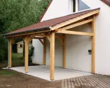 Un abri de voiture en bois avec une pente légère, adossé à une maison blanche.