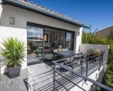 Terrasse sur le toit accessible, avec table et chaises, et une grande baie vitrée donnant sur un salon rempli de livres.