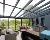 Salon moderne avec un toit en verre laissant entrer la lumière. Des canapés confortables invitent à la détente, tandis que le jardin verdoyant offre une vue paisible.