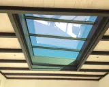 Veranda avec un grand puit de lumière vitré, illuminant un plafond en bois et poutres métalliques.