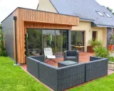 Une extension bois 30m2 moderne avec terrasse en bois, mobilier de jardin et grandes baies vitrées.