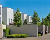 Lignes architecturales modernes, une extension accolée sur mur non mitoyen, des arbres et des voitures garées dans des box.