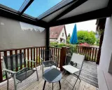 Un petit veranda balcon avec des chaises et une table, offrant une vue sur un jardin verdoyant et une maison.