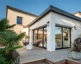 Une extension verrière moderne illumine cette maison ancienne, offrant une vue imprenable sur la terrasse en bois et le jardin luxuriant.