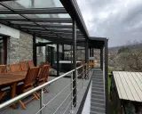 Veranda sur terrasse surélevée avec jacuzzi et table en bois. Vue sur un village et des collines brumeuses.