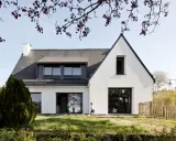 Une extension maison néo-bretonne moderne avec de grandes baies vitrées. Deux enfants jouent dans le jardin verdoyant devant la maison.