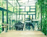 Un charmant jardin d'hiver verrière, avec des tables et chaises en fer forgé, une statue d'ange et une profusion de verdure.