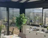 Intérieur lumineux d'une véranda triple vitrage, avec vue sur un jardin verdoyant et une commode blanche décorée.