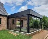 Moderne véranda toit plat avec puits de lumière, offrant une vue panoramique sur le jardin. L'extension en verre et métal s'intègre parfaitement à la maison en briques.