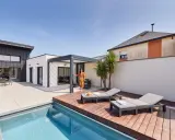 Une femme en robe colorée se tient près d'une pergola moderne, profitant de l'étanchéité pergola mur. Piscine et chaises longues complètent ce paysage de détente.