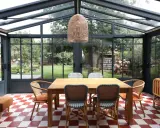 Salle à manger lumineuse dans une véranda extension, avec table en bois, chaises colorées et vue sur le jardin.