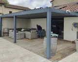 Installation d'un auvent sans permis de construire. Un homme arrange des coussins sur un canapé extérieur sous la structure moderne.